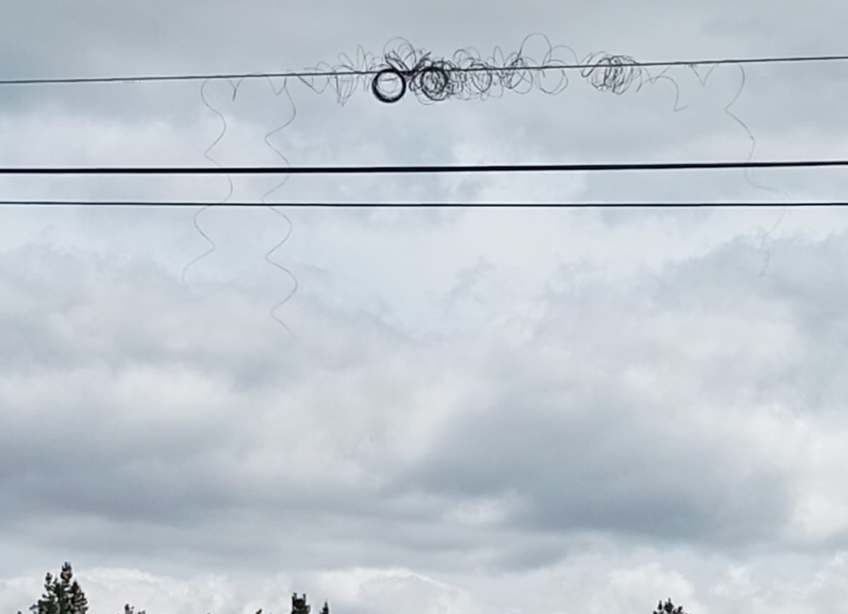 Restos de fibra óptica enredados nunha liña aérea sobre o rural galego, tras unha instalación deficiente.